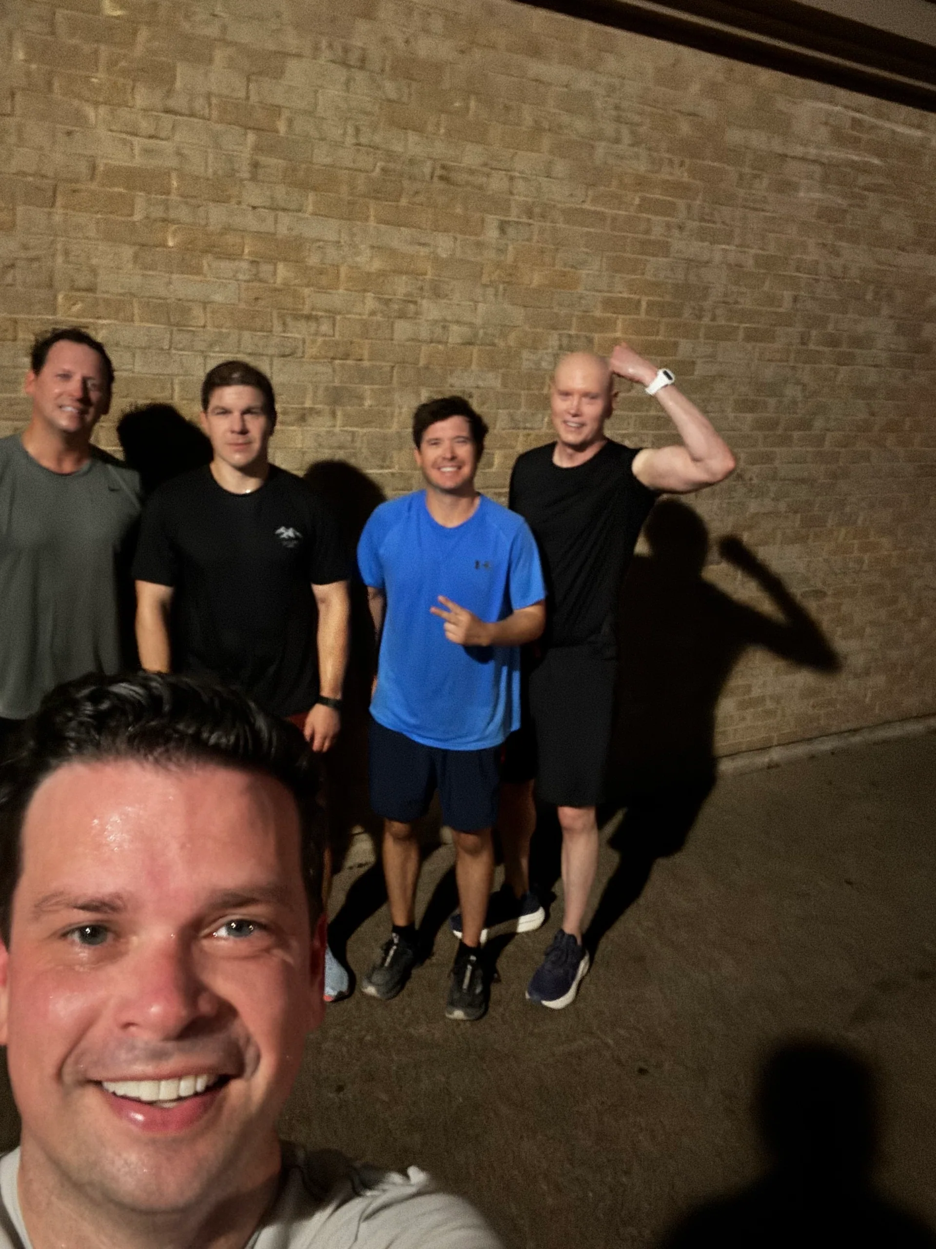 F3 Dallas members taking a group selfie beside a brick wall at night